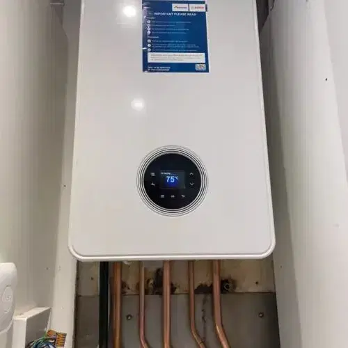 A modern gas boiler installed in a utility room, featuring a digital display and pipes
